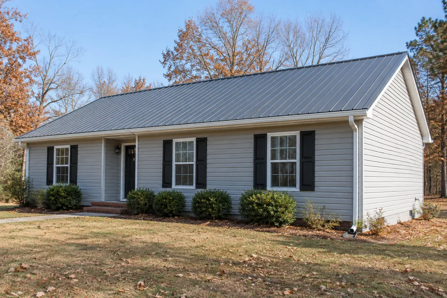 Illustrative single-story home with a gray metal gable roof, white eave gutter, and corner downspout in a dry autumn setting.